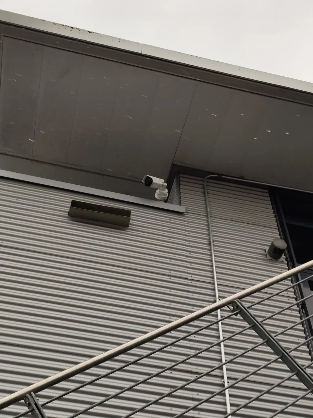 Bispektrale Thermal-PTZ-Überwachungskamera mit integriertem IR-Scheinwerfer an einer Firmenfassade in großer Höhe – typischer Bestandteil eines 10-Kamera-Systems für Gewerbeobjekte