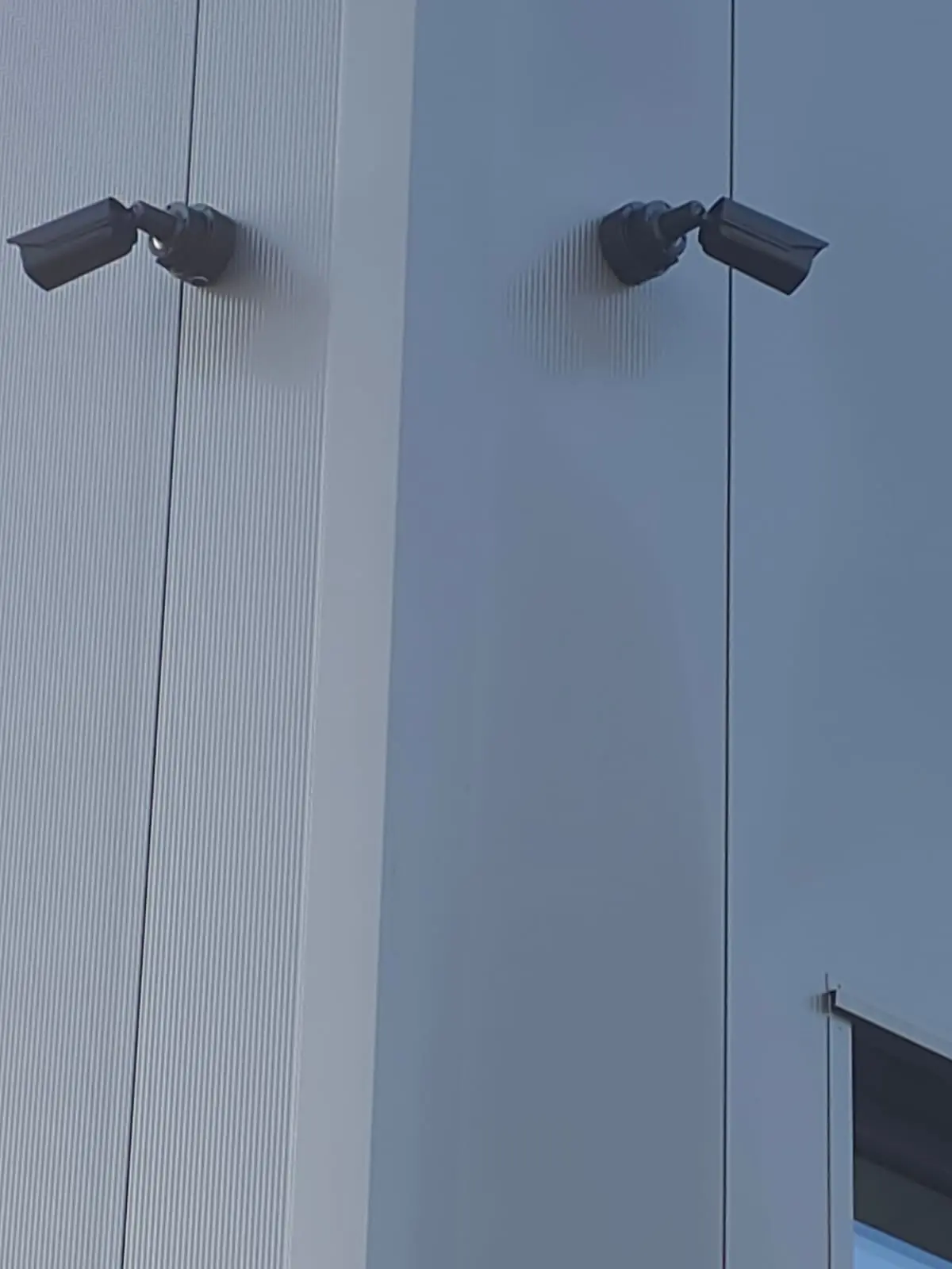 Zwei Bullet-Überwachungskameras in Doppelmontage an einer Firmenfassade mit Stahlblech-Verkleidung – typische Ecklösung für lückenlose Abdeckung bei einem 10-Kamera-System