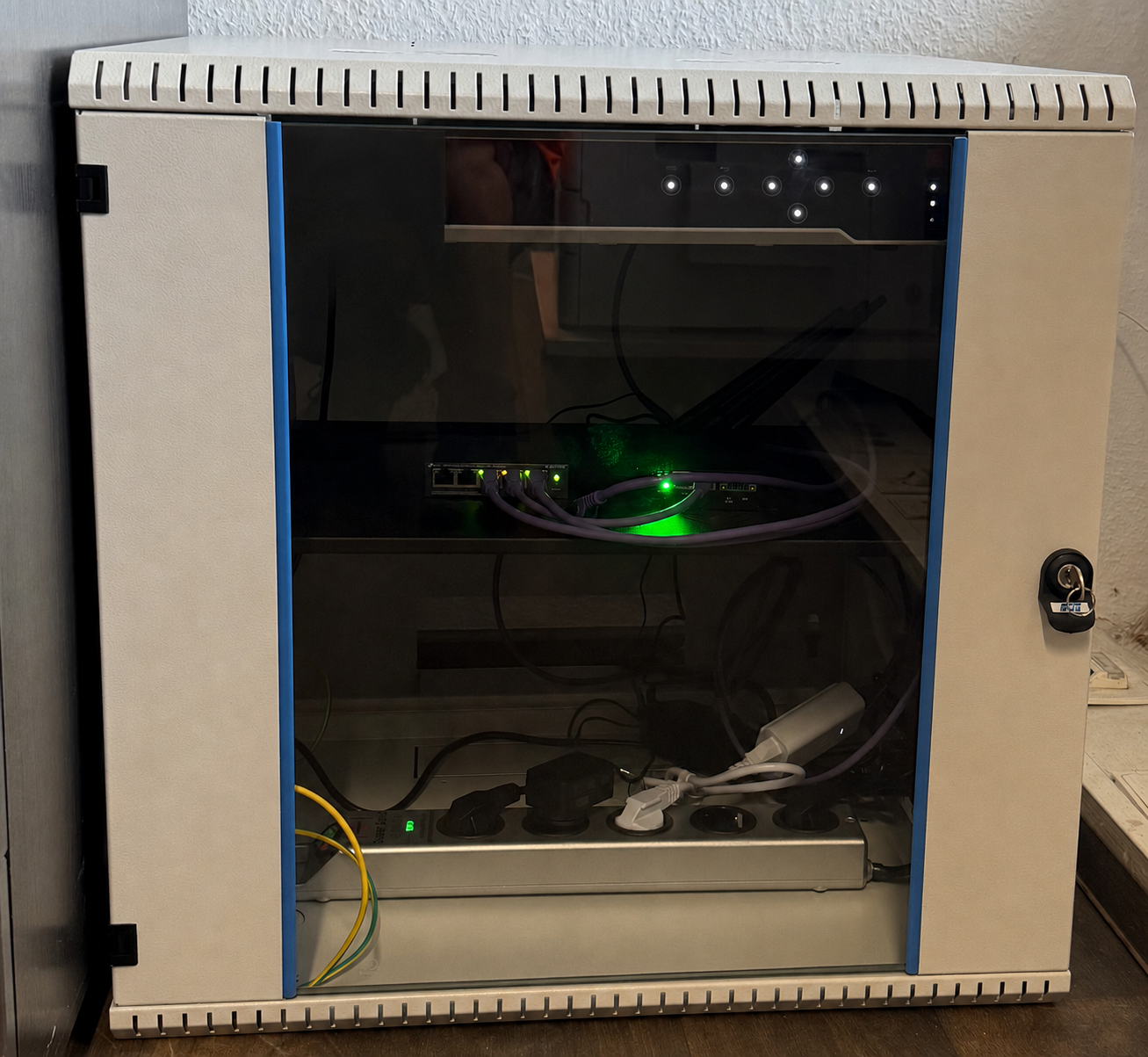 Netzwerkschrank mit PoE-Switch, NVR und USV – verkabelt mit grauen Cat6-Patchkabeln, aktive Link-LEDs leuchten grün (Beispiel-Installation OBJEXA)