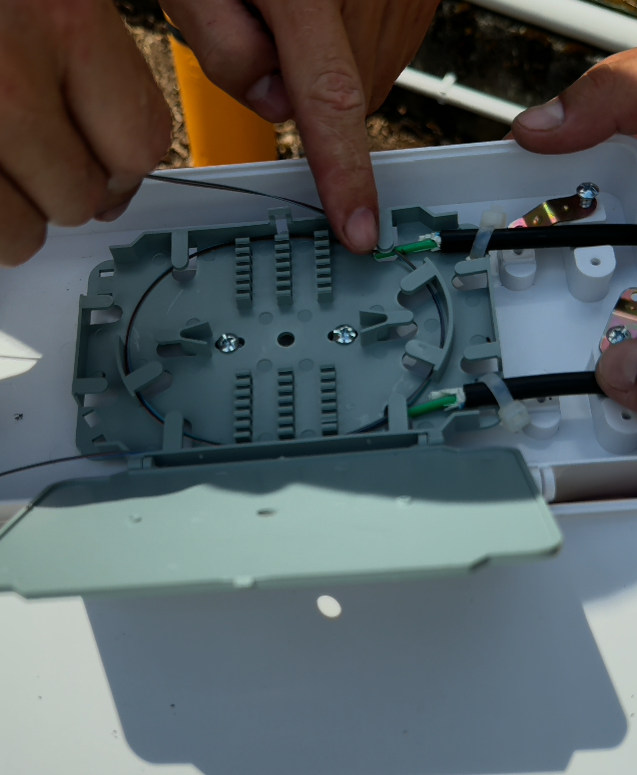 Mid-Span-Zugang an einem LWL-Glasfaserkabel: geöffnete Spleißkassette mit Pufferröhrchen und freigelegten Fasern während der Techniker-Installation im Außenbereich