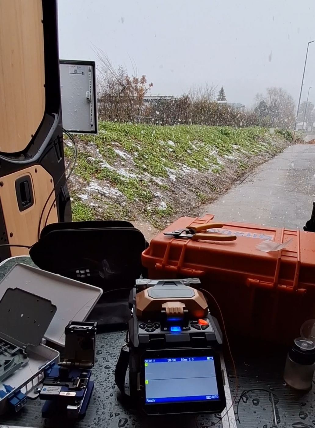 Glasfaser-Spleißeinsatz im Schnee: Fusion Splicer, Cleaver und Werkzeugkoffer im offenen Servicebus eines CCTV-Technikers